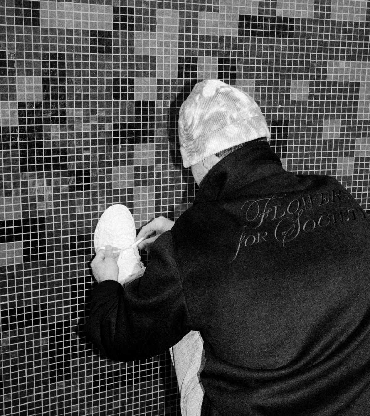 Person wearing black Jacket with Flowes for Society print on back tying Radicle OG sneaker