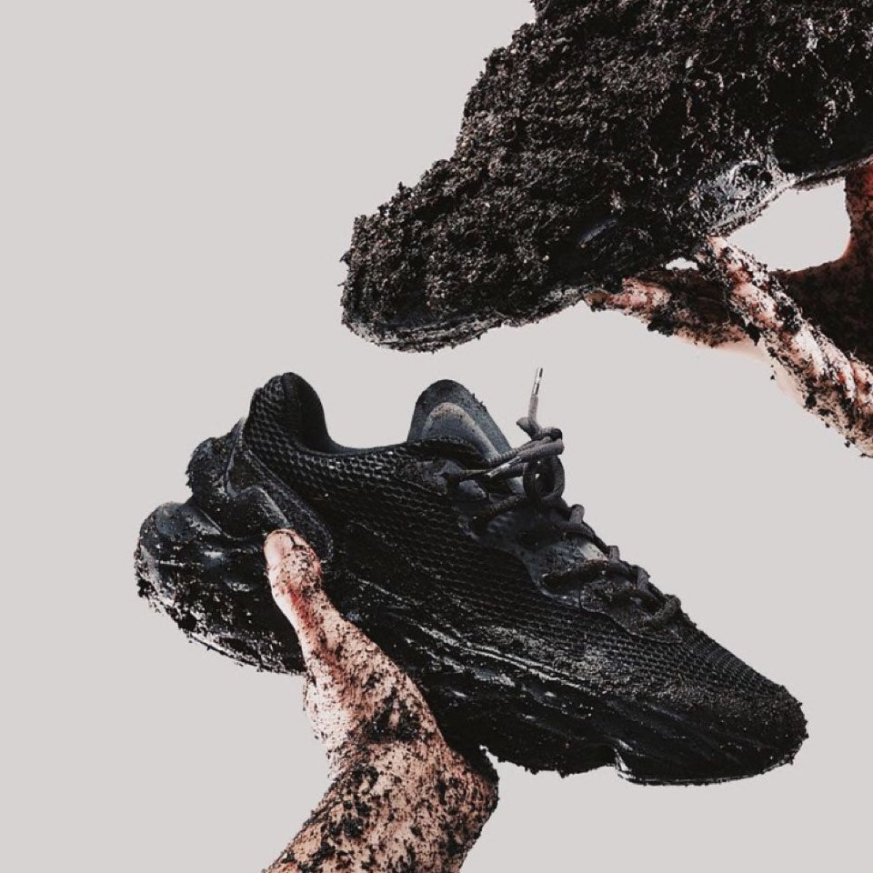 Campaign picture of the Seed.One Black Mud with muddy hands and the shoes on a grey background