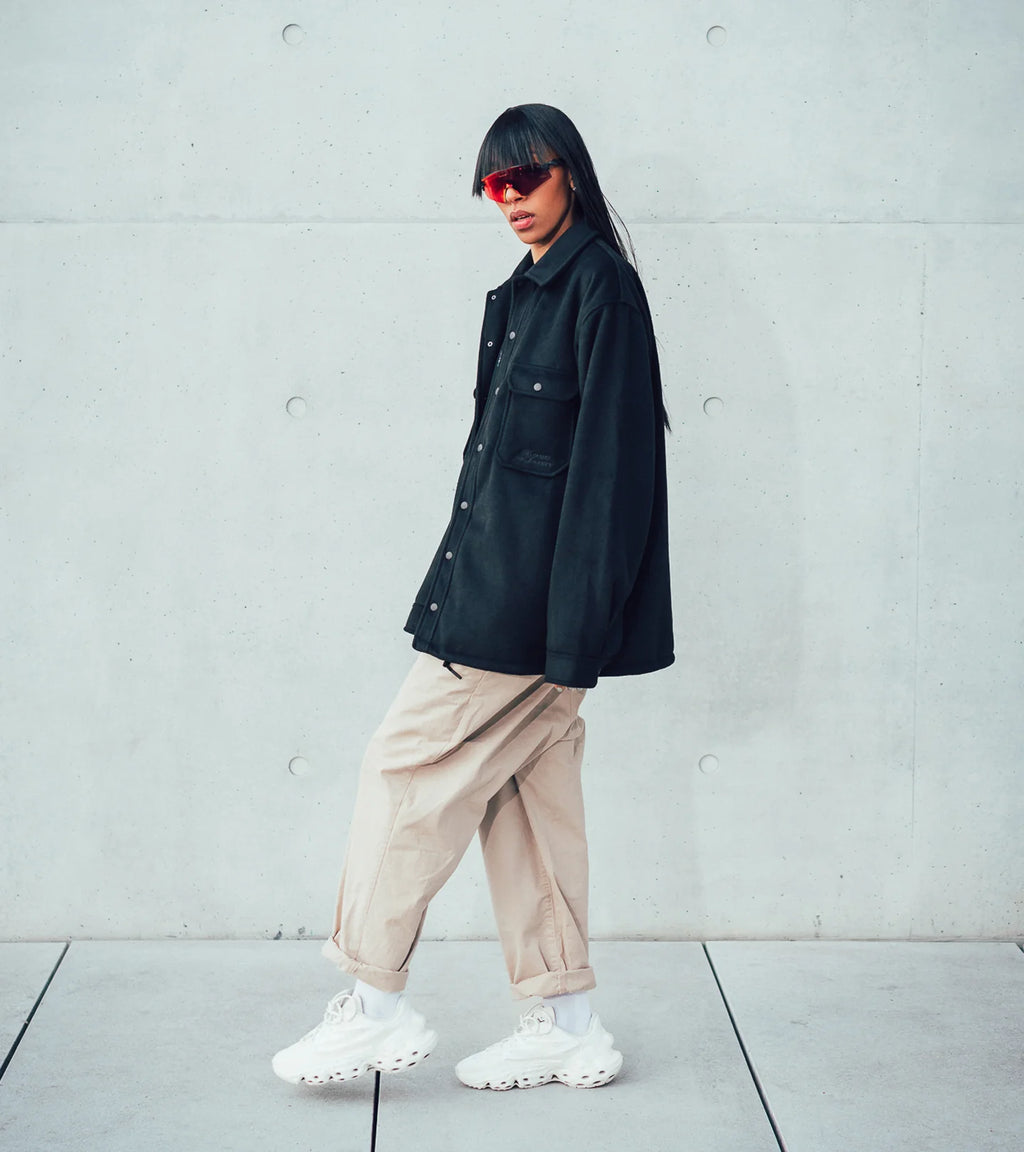 A model posing in side view in the Bouquet Collection jacket and the Seed.One White Lily in front of a concrete building