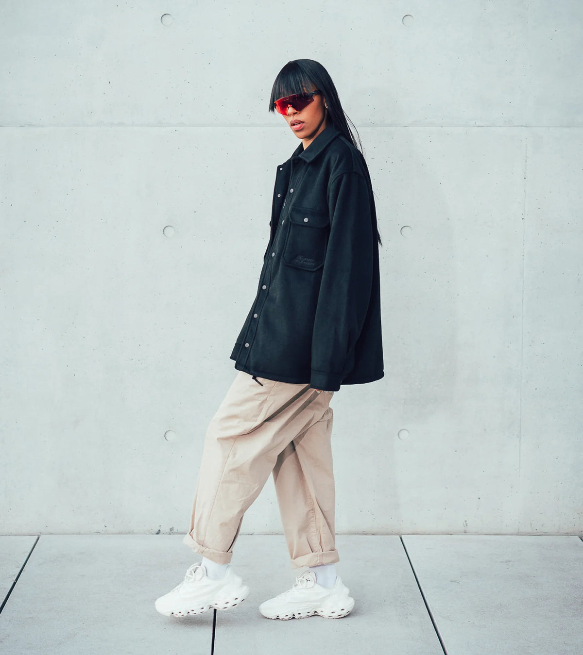 A model posing in side view in the Bouquet Collection jacket and the Seed.One White Lily in front of a concrete building