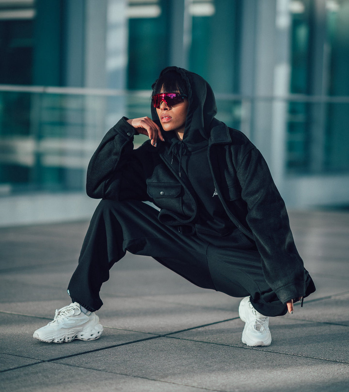 A model on a concrete plateau in front of a glass building wearing apparel from the Bouquet Collection and the Seed.One White Lily on foot